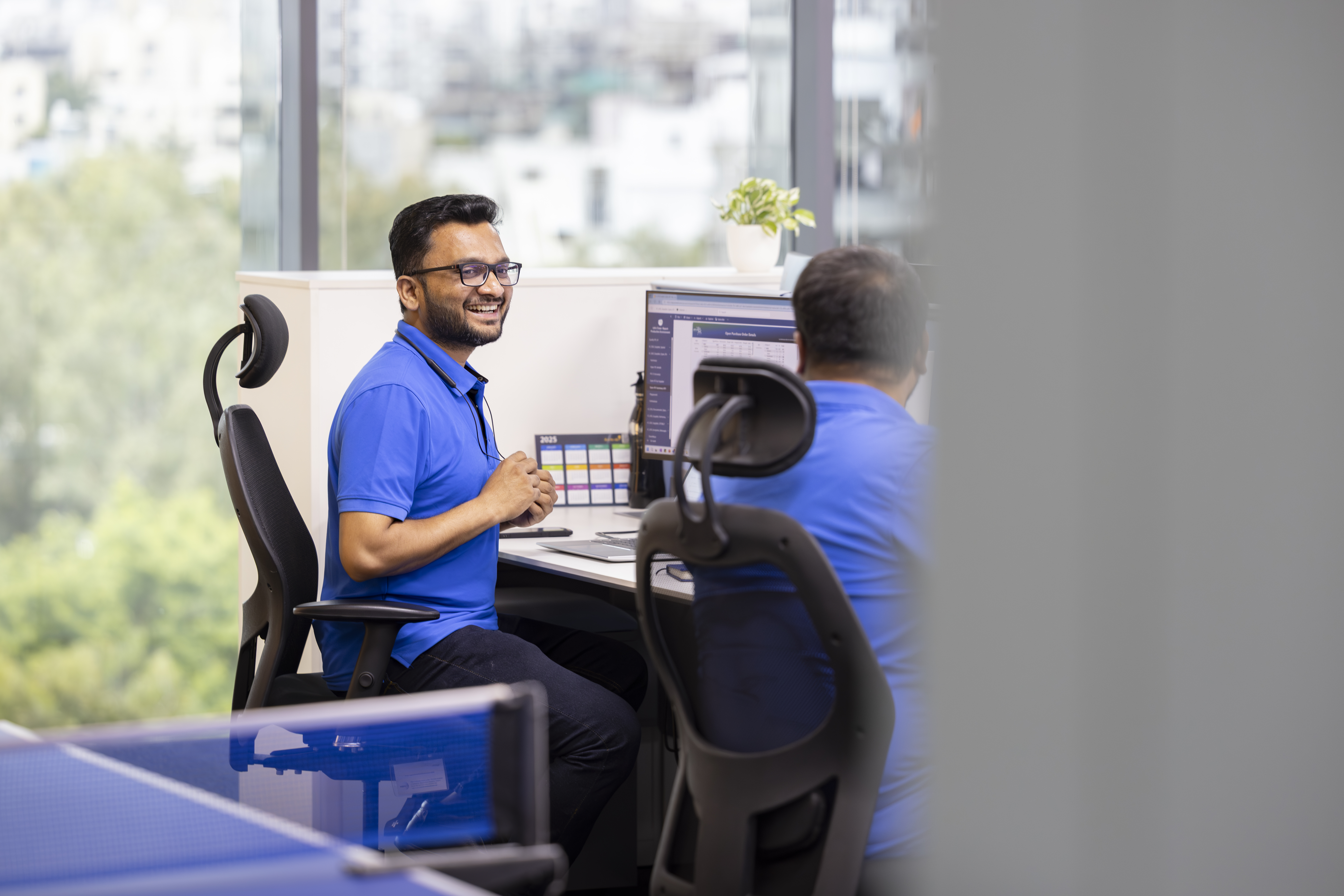 Employee In Blue Tshirt Sitting At Computer Smiling At A Colleague
