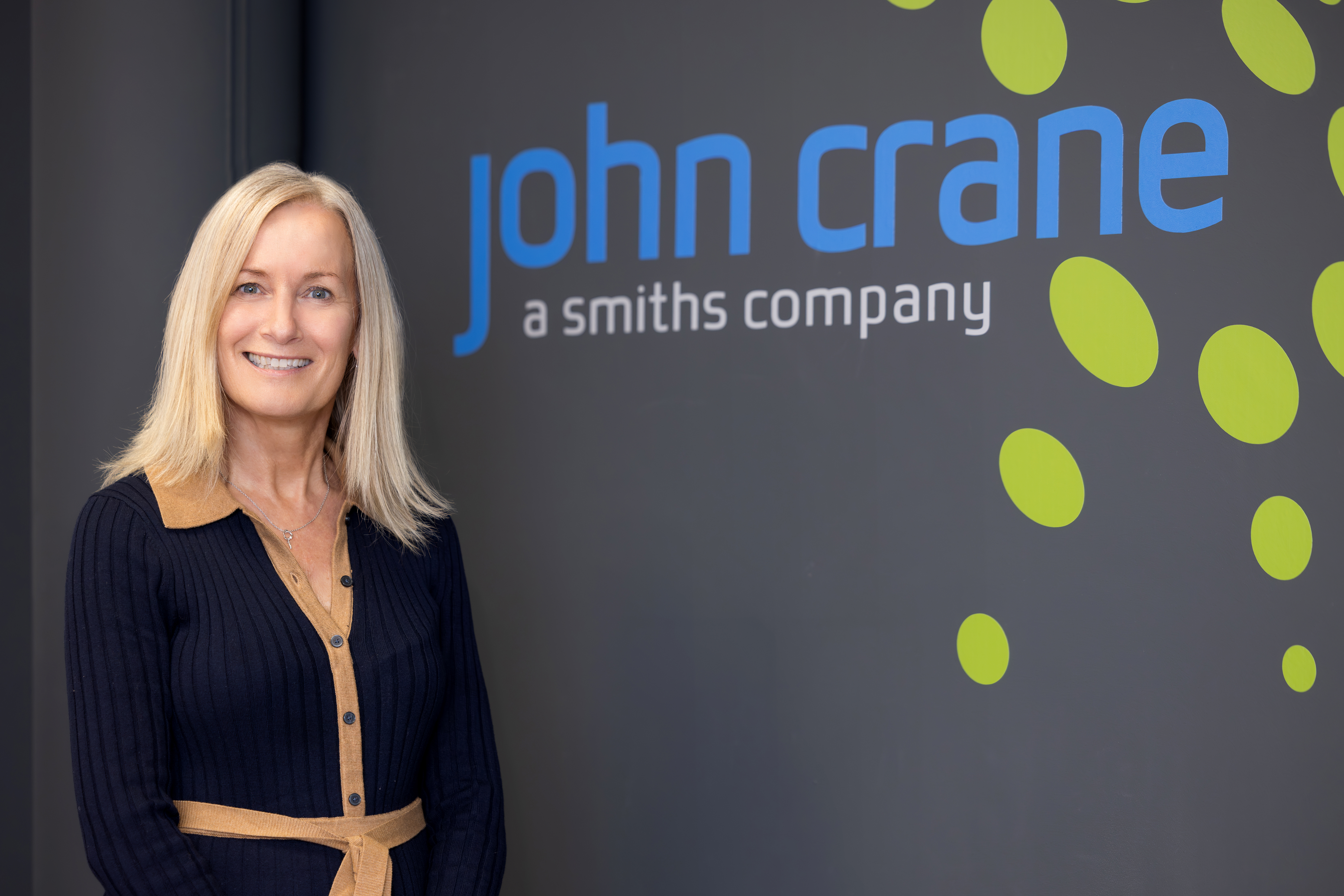 Smiling Woman Standing In Front Of Wall With John Crane Logo On It